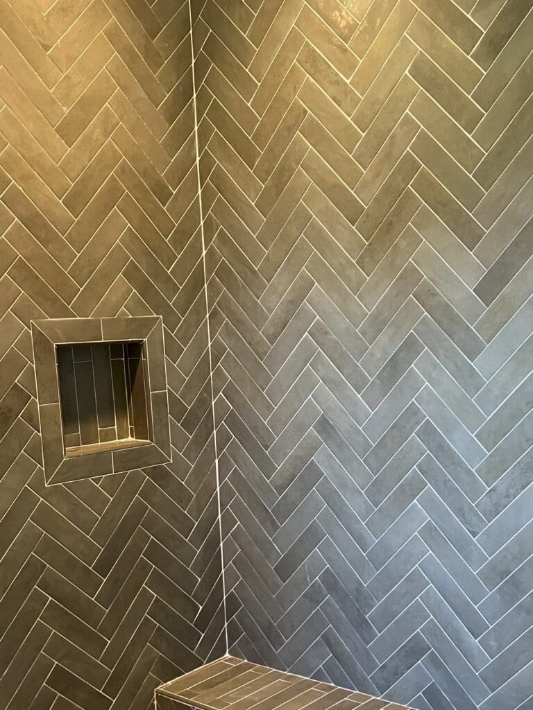 Gray herringbone tiled shower corner with niche